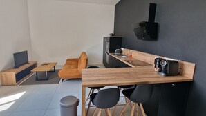 Een moderne woonruimte met een bank, salontafel, televisie, keuken met een magnetron, en een wandluidspreker.
