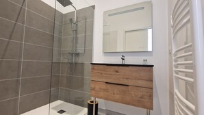 Een moderne badkamer met een douche met glazen wand, een houten wastafelmeubel met spiegel en een witte radiator.