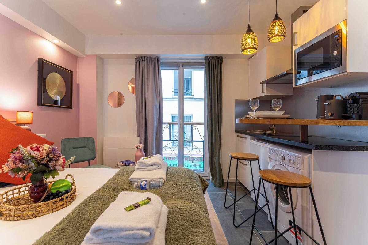 Una habitación de hotel moderna con cama, zona de comedor, cocina y vistas a la ciudad.