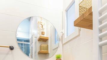 A modern bathroom with a round mirror, a white sink, wooden shelves, and a towel rack.