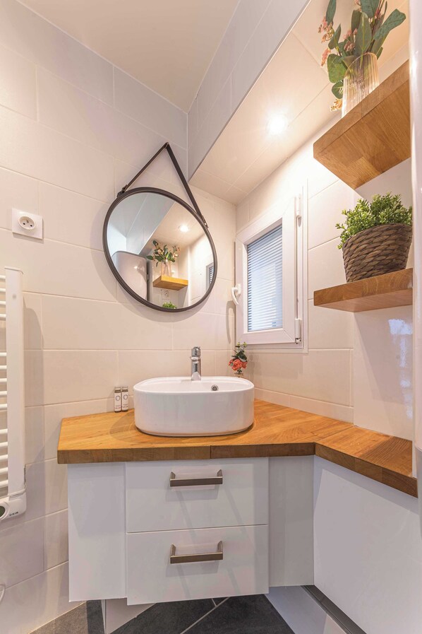 A modern bathroom with a round mirror, wooden countertop, and built-in shelves. - Résidence Paris 58 BEAUREGARD (Paris)