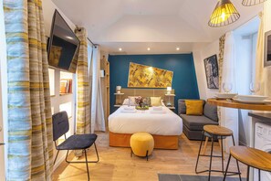 A modern bedroom with a large bed, a sofa, a small dining area, and a TV mounted on the wall. - Résidence Paris 58 BEAUREGARD (Paris)