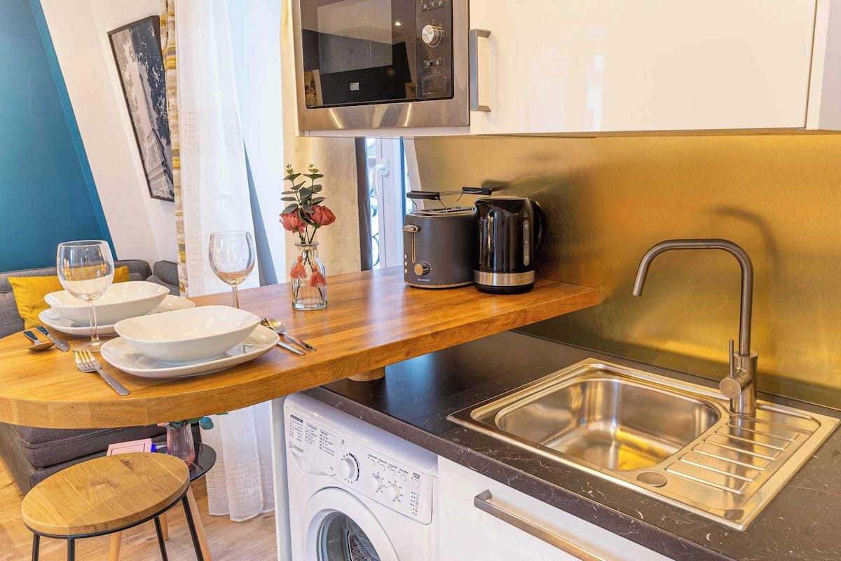 Una kitchenette compacta con microondas, tostadora, hervidor y un lavamanos de acero inoxidable.