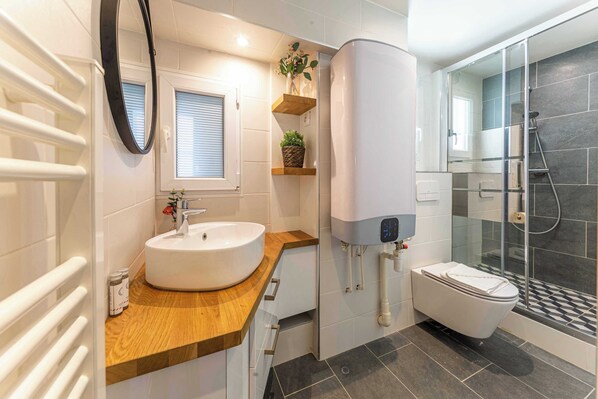 A modern bathroom with a round sink, a toilet, a glass shower enclosure, and a built-in heater. - Résidence Paris 58 BEAUREGARD (Paris)