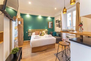 A modern bedroom with a large bed, a small sitting area, and a kitchenette. - Résidence Paris 58 BEAUREGARD (Paris)