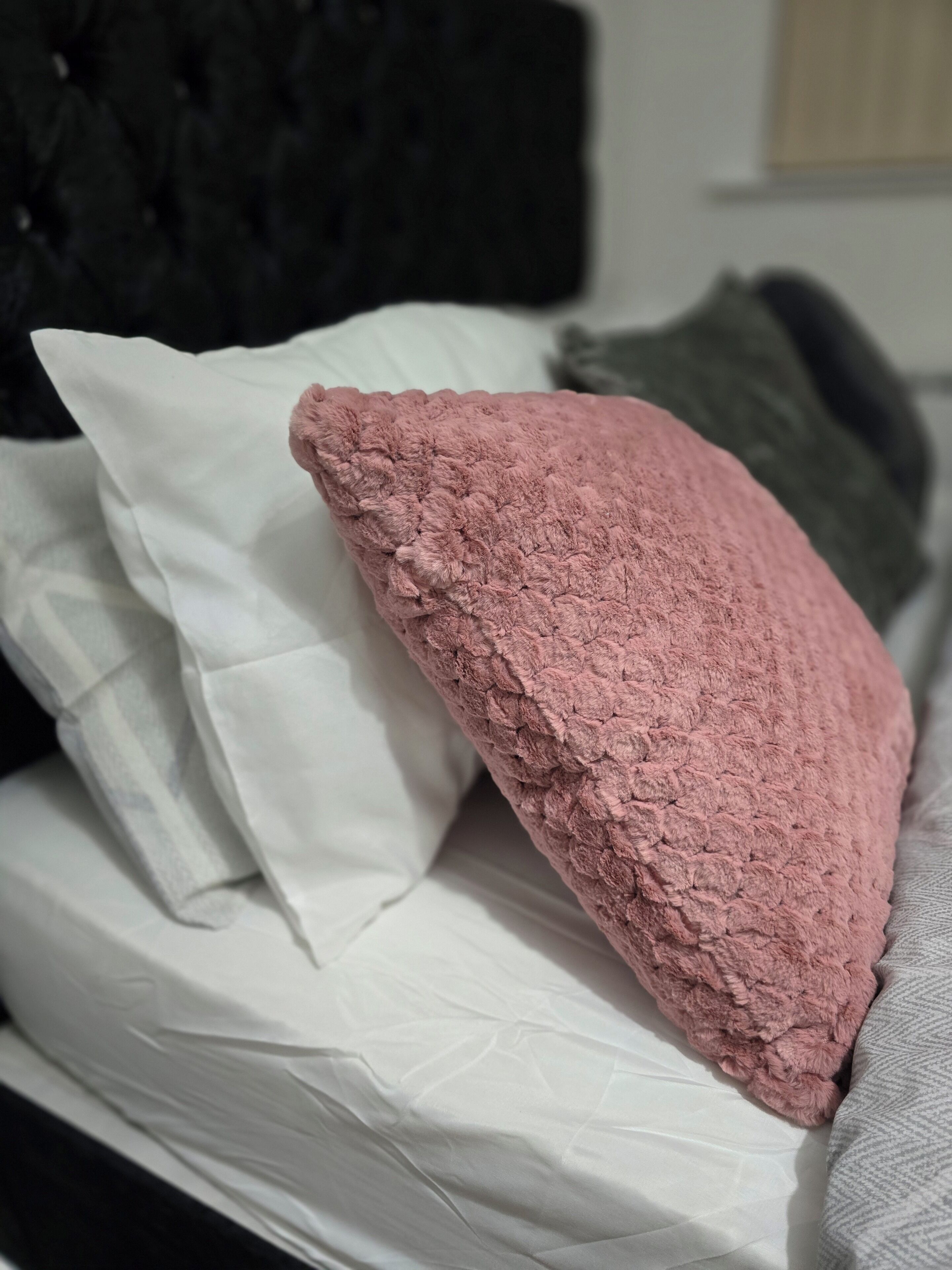 Een bed met een witte matras, een roze kussen met textuur en een grijs kussen.