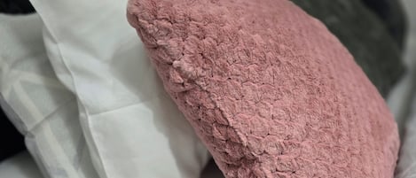 A bed with a white mattress, a pink textured pillow, and a grey pillow.