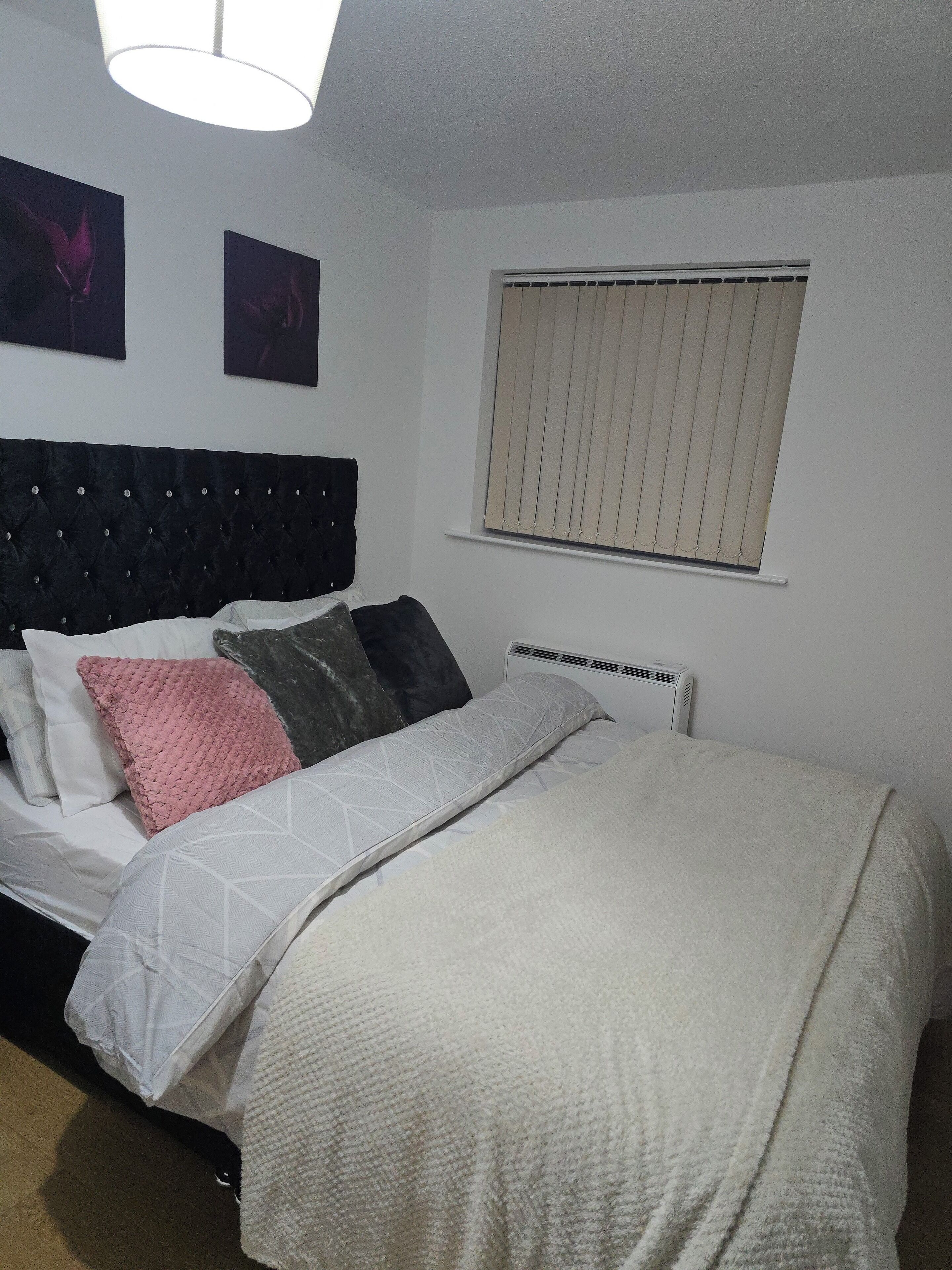 Een slaapkamer met een bed, een radiator en een raam met jaloezieën.