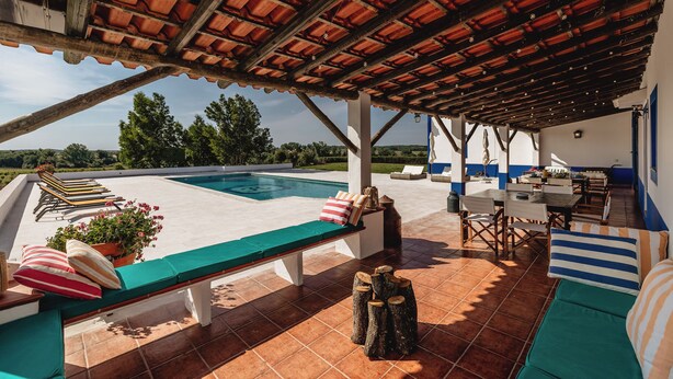 A covered outdoor area with a pool, lounge chairs, and seating.