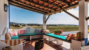 A covered outdoor seating area with a view of vineyards.