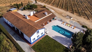 An aerial view of a property with a swimming pool, a large house with a tiled roof, and a well-maintained lawn.
