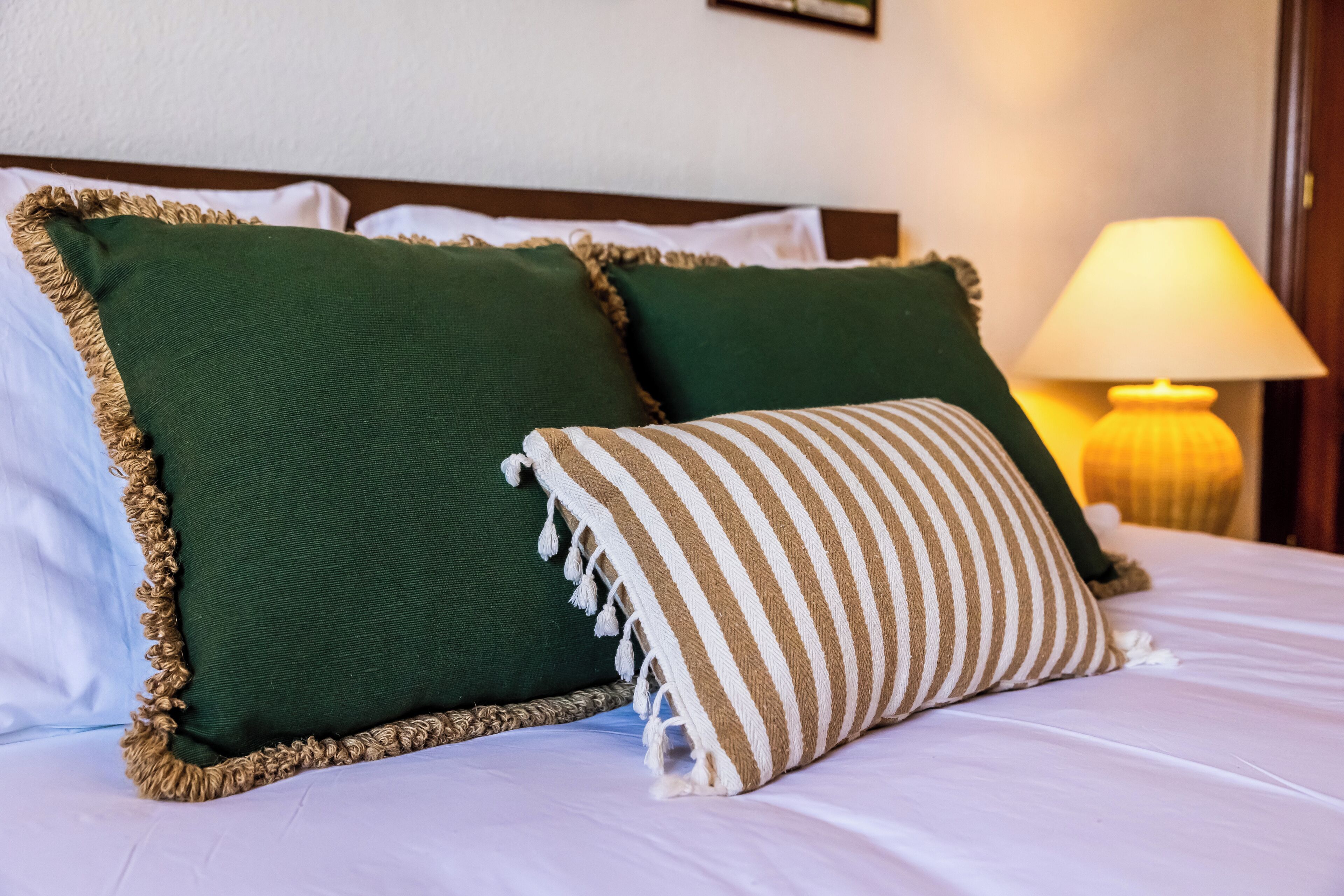 A bed with green pillows and a striped pillow, a lamp, and a wooden headboard.