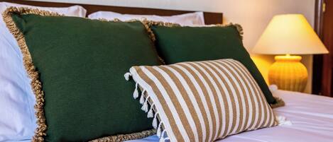 A bed with green pillows and a striped pillow, a lamp, and a wooden headboard.