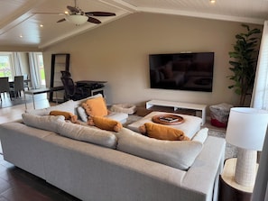 Ein modernes Wohnzimmer mit einem großen Sofa, einem Flachbildfernseher, einem Deckenventilator und einem Essbereich mit Tisch und Stühlen.