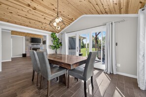 Una cucina moderna con una TV a schermo piatto, un'area pranzo con tavolo in legno e sedie grigie, e un'ampia porta scorrevole in vetro che dà su un giardino.