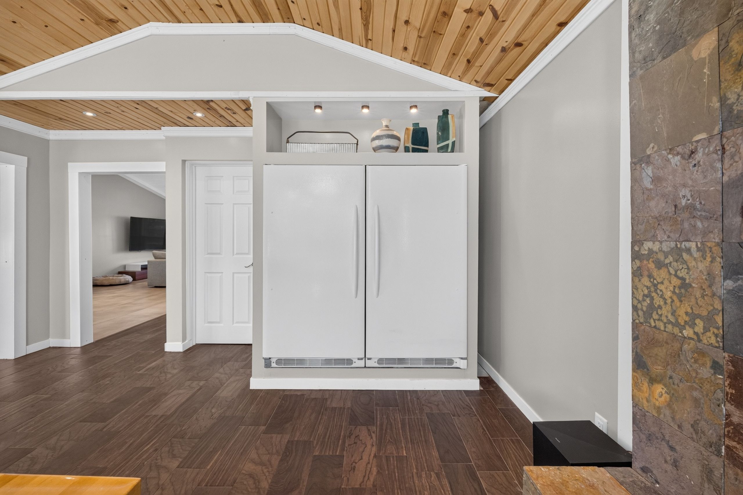 Une cuisine moderne avec des meubles blancs, un plafond en bois et un mur d’accent en pierre.