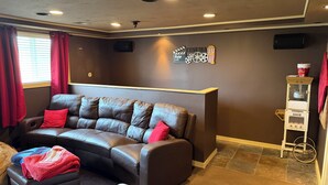 A living room with a leather sofa, a small ottoman, a red blanket, a cinema-themed wall decoration, and a candy dispenser. - Sleeps 10/Batting Cage/Theater! (Westfield)