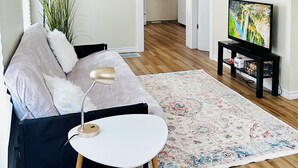 A modern living room with a sofa, a small white table, a floor lamp, a TV on a stand, and a patterned rug. - Spacious 2BR House with Netflix, BBQ, and Patio Near City Centre (Peterborough)