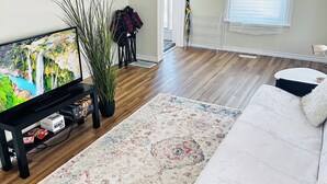 A living room with a flat-screen TV, a large rug, a sofa, and a potted plant. - Spacious 2BR House with Netflix, BBQ, and Patio Near City Centre (Peterborough)