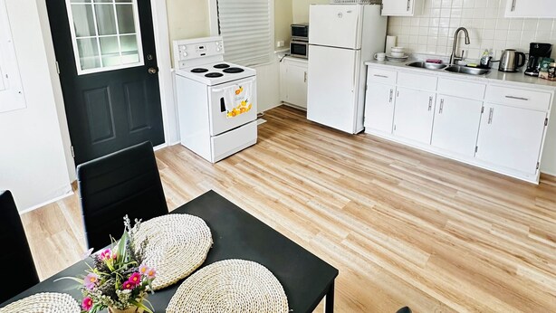A modern kitchen with white cabinets, a black countertop, and a dining area with a black table and woven placemats. - Spacious 2BR House with Netflix, BBQ, and Patio Near City Centre (Peterborough)