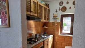 Une cuisine compacte avec des meubles en bois, une cuisinière à gaz, un évier et une fenêtre donnant sur l’extérieur.
