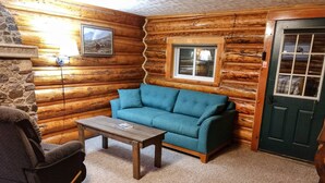 Interior acogedor de una cabaña de madera con un sofá azul, una mesa de centro de madera y una chimenea de piedra.