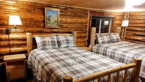 Un dormitorio tipo cabaña de madera con dos camas, cabeceros de madera, un cuadro en la pared y dos lámparas de noche.