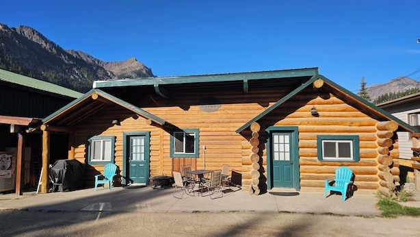 Una cabaña de troncos con dos puertas, un porche cubierto con sillas y un letrero que dice "Cabins".