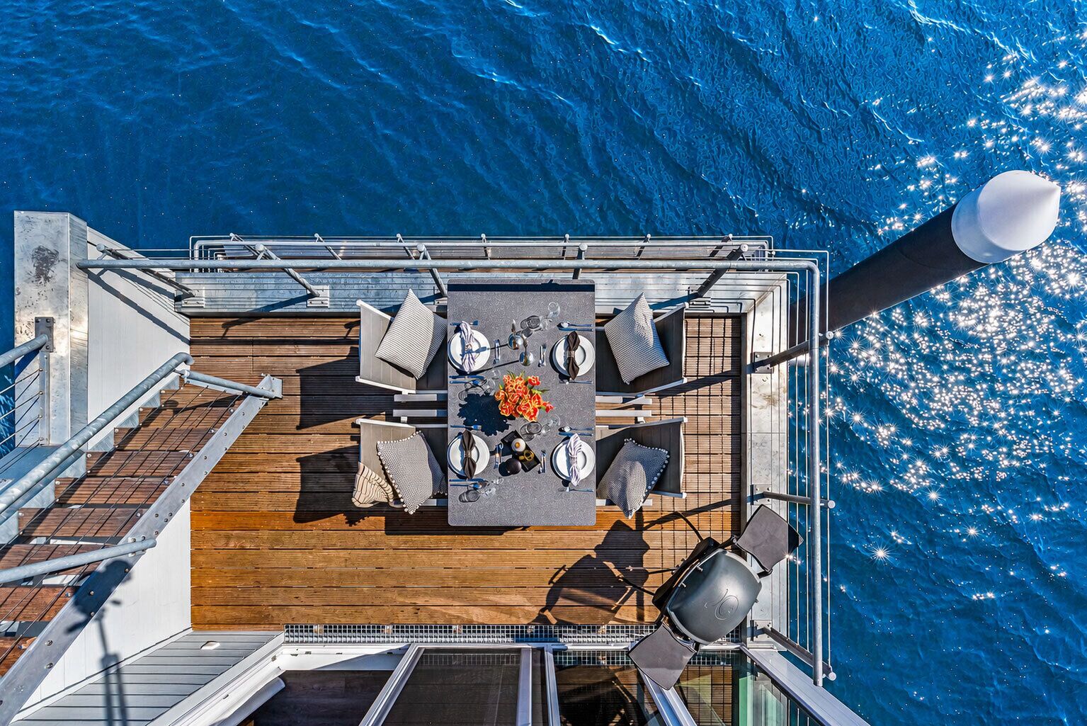 An aerial view of a deck with a dining table, chairs, and a ship's wheel.