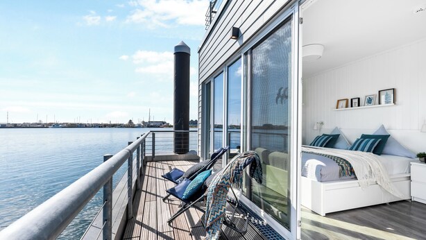 En balkon med udsigt over vandet, en seng med puder og et gelænder.