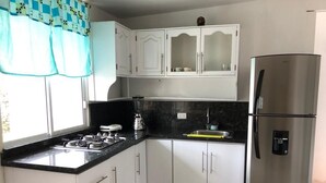 Een keuken met witte kastjes, een zwart aanrecht, een roestvrijstalen koelkast en een raam met gordijnen.