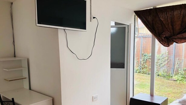 Een slaapkamer met een aan de muur bevestigde televisie, een bed met een gebedrukte spreidek, een klein tafeltje met een stoel en een schuifdeur naar een balkon.