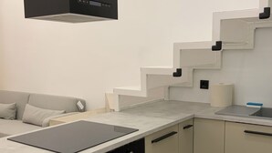 A modern kitchen with a built-in oven, a black countertop, and a grey sofa.