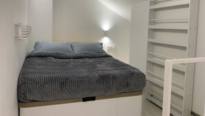 A bedroom with a bed, a nightstand, a wall-mounted light, and a built-in shelving unit.