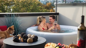 Un couple dans un jacuzzi, avec un chien à proximité, entouré de collations et d’une bouteille.