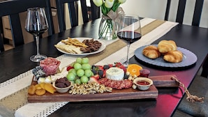 Une table à manger dressée avec une variété de fromages, de fruits, de noix et de pâtisseries, accompagnée de verres de vin rouge.
