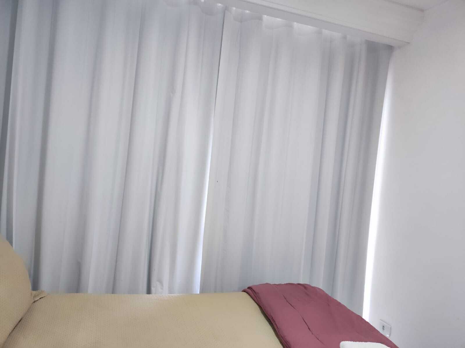 A hotel room with a bed, a red blanket, and sheer white curtains.