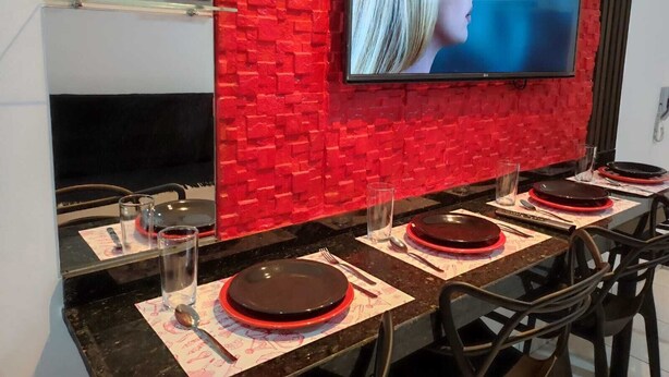 Een moderne eetruimte met een rode baksteenmuur, een flatscreen televisie boven de balie en een tafel gedekt met borden, glazen en bestek.