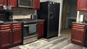A kitchen with wooden cabinets, a stainless steel refrigerator, a microwave, a stove, and a coffee maker. - 5BR Home w/ Game & Fitness Rooms 15 Mins to Ft Benning. (Phenix City)