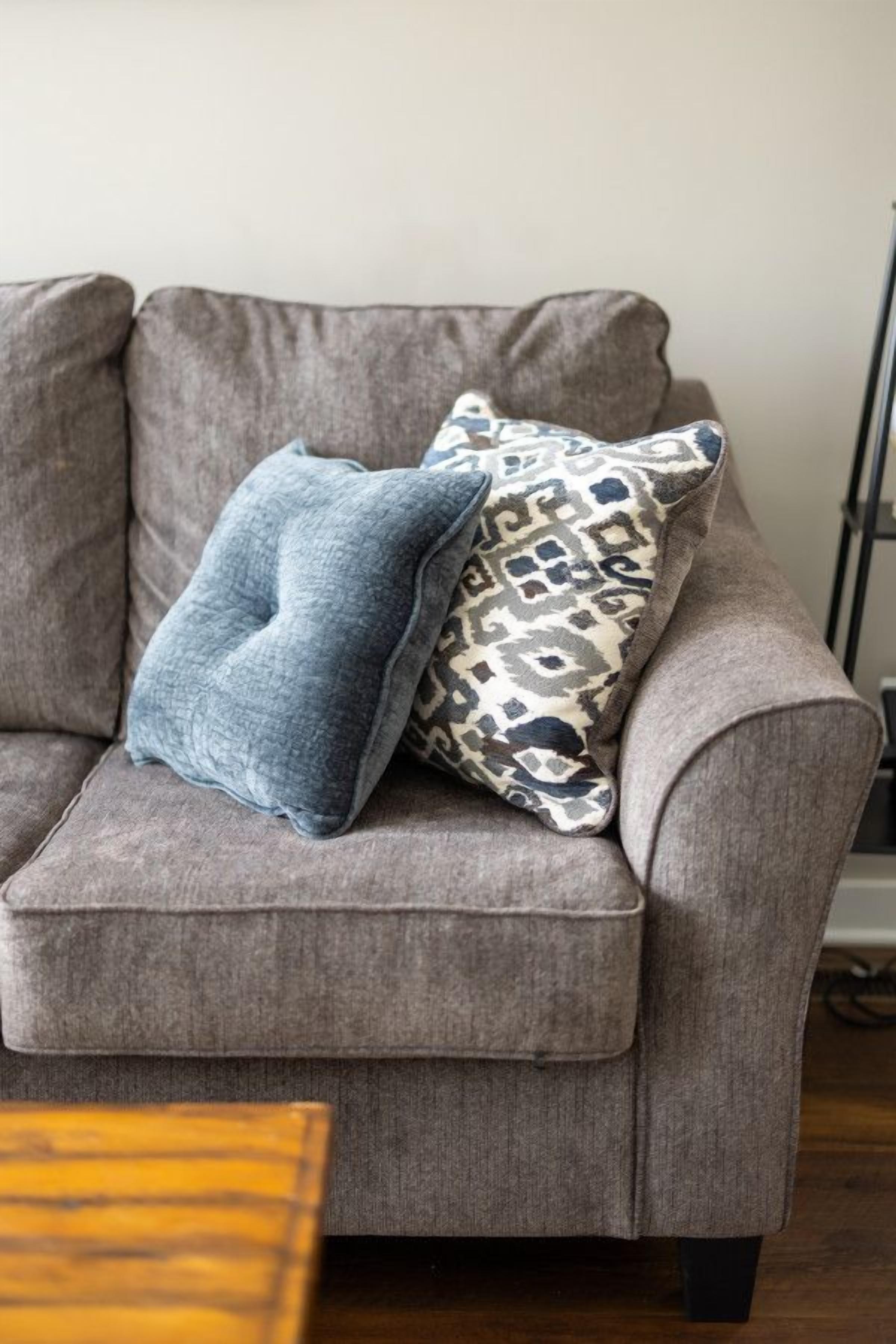 Un sillón gris con un cojín estampado y un cojín azul liso.
