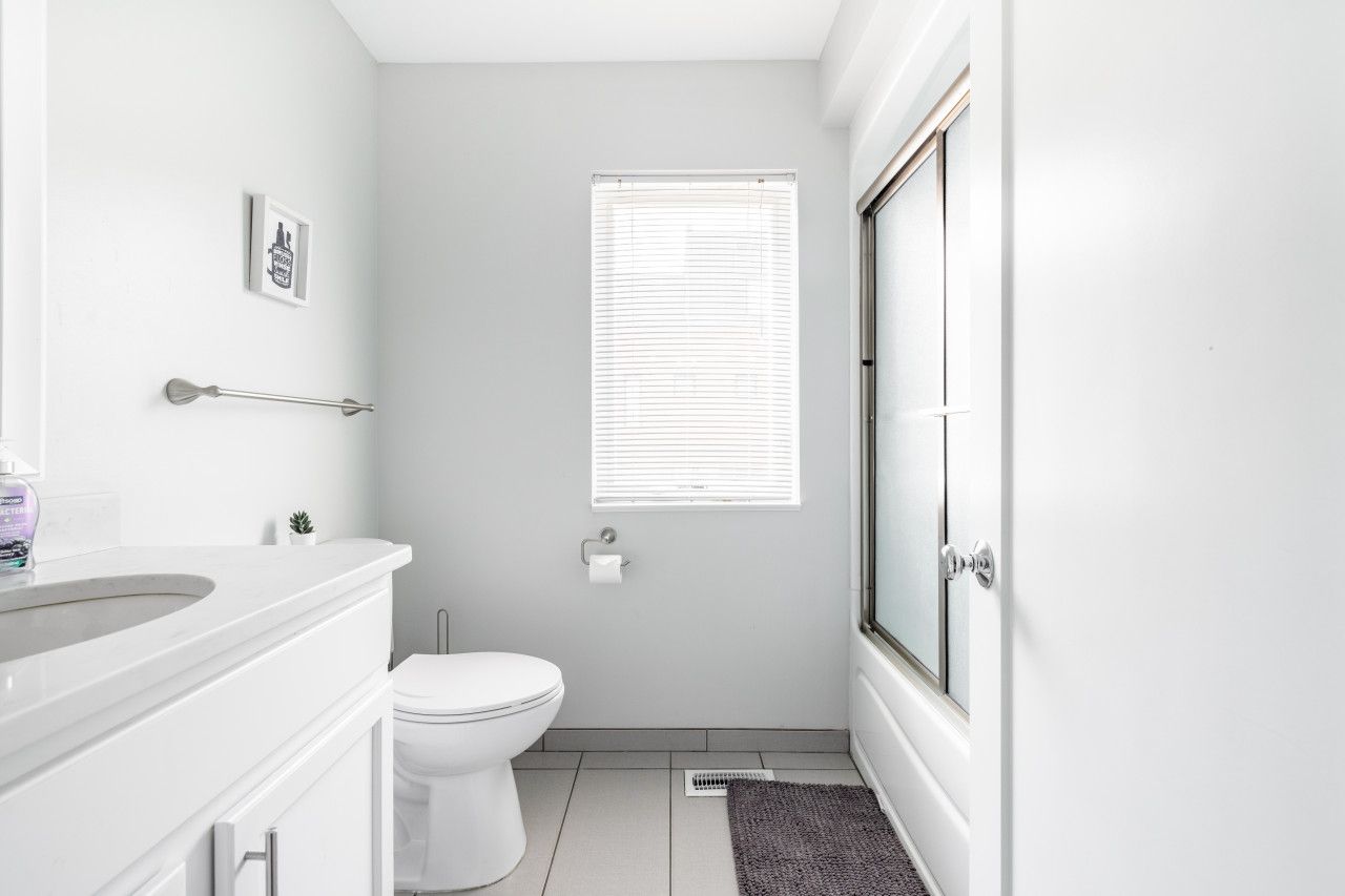 A compact bathroom with a toilet, a sink, a small window with blinds, and a shower area.