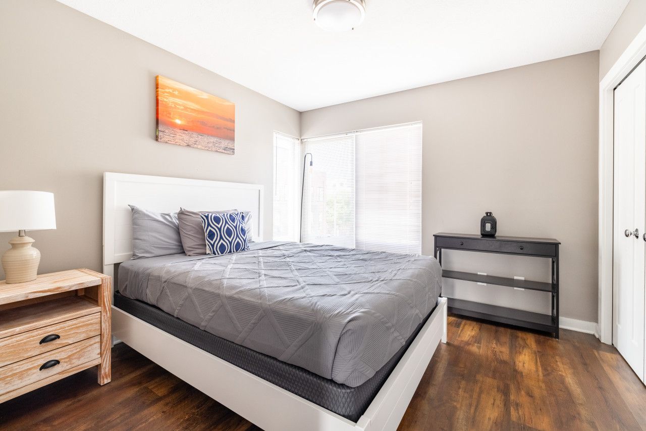 A bedroom with a bed, bedside table, nightstand, and a painting on the wall.