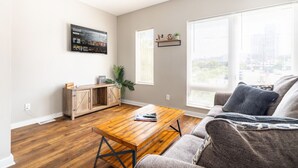 A living room with a wooden coffee table, grey sofa, and a small cabinet with a plant. - Luxury Downtown Townhome w/ Private Garage Unit 16 (Cleveland)