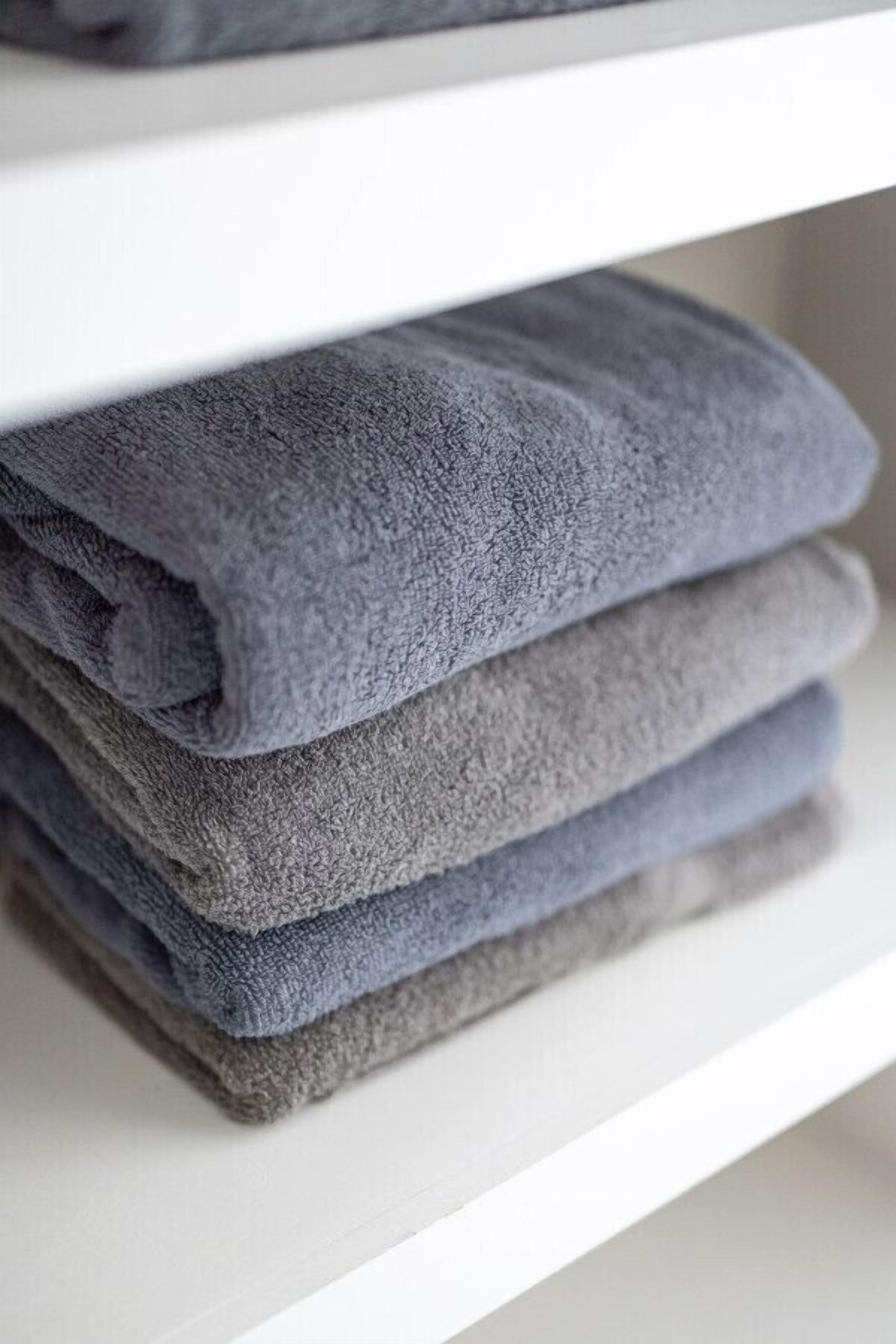 A stack of folded towels on a white shelf.