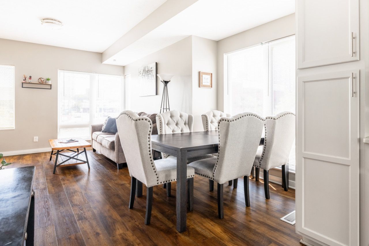 A dining area with a dark wooden table surrounded by upholstered chairs with button details, a light-colored sofa, and a floor lamp.