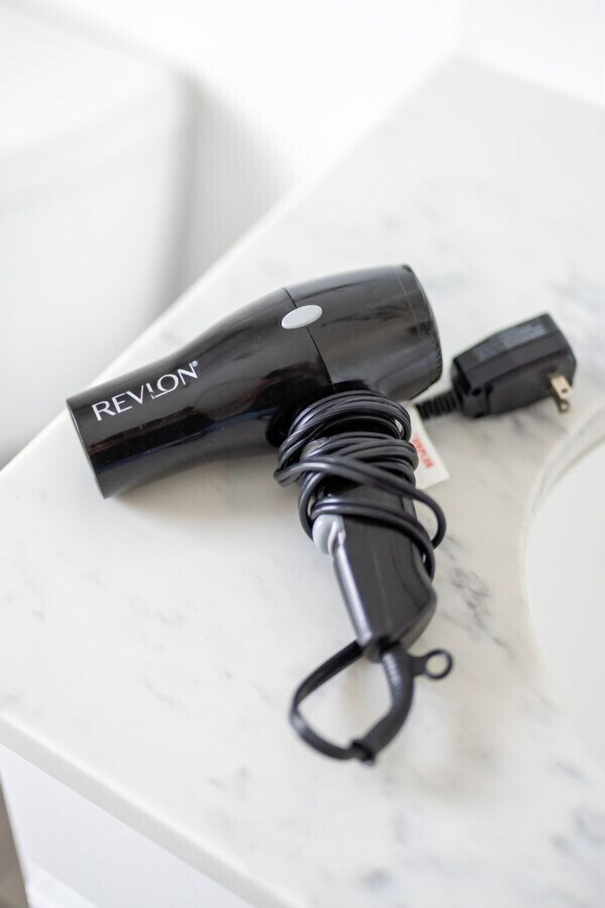 A black Revlon hair dryer with a cord and a power adapter on a white marble surface.