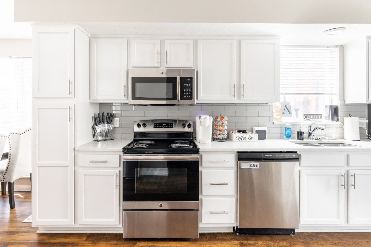 Una cocina moderna con armarios blancos, microondas, estufa y lavavajillas de acero inoxidable.