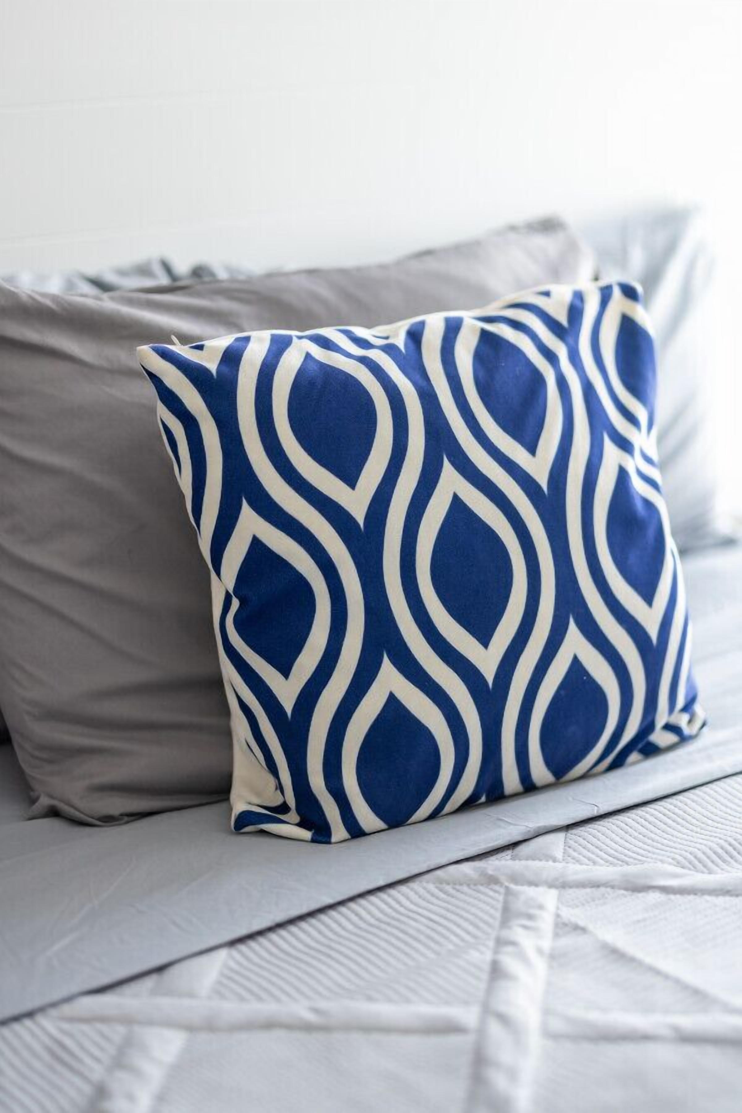 A bed with a blue and white patterned pillow and a plain gray pillow.