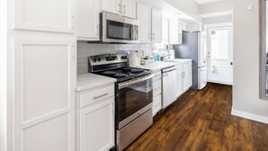 A modern kitchen with white cabinetry, stainless steel appliances, and a wooden floor. - Luxury Downtown Townhome w/ Private Garage Unit 16 (Cleveland)