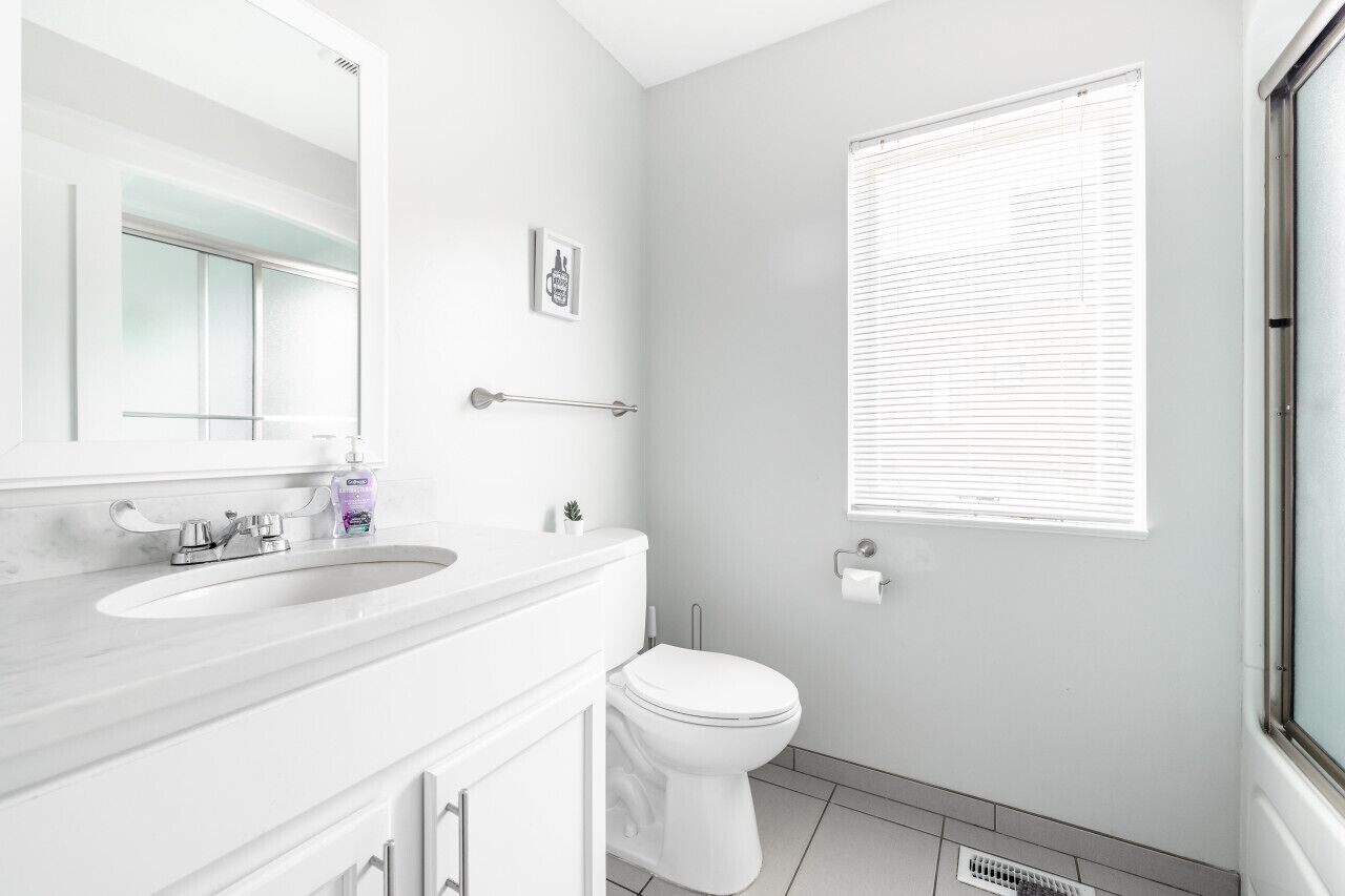 Un baño moderno con lavamanos, espejo y inodoro blancos.